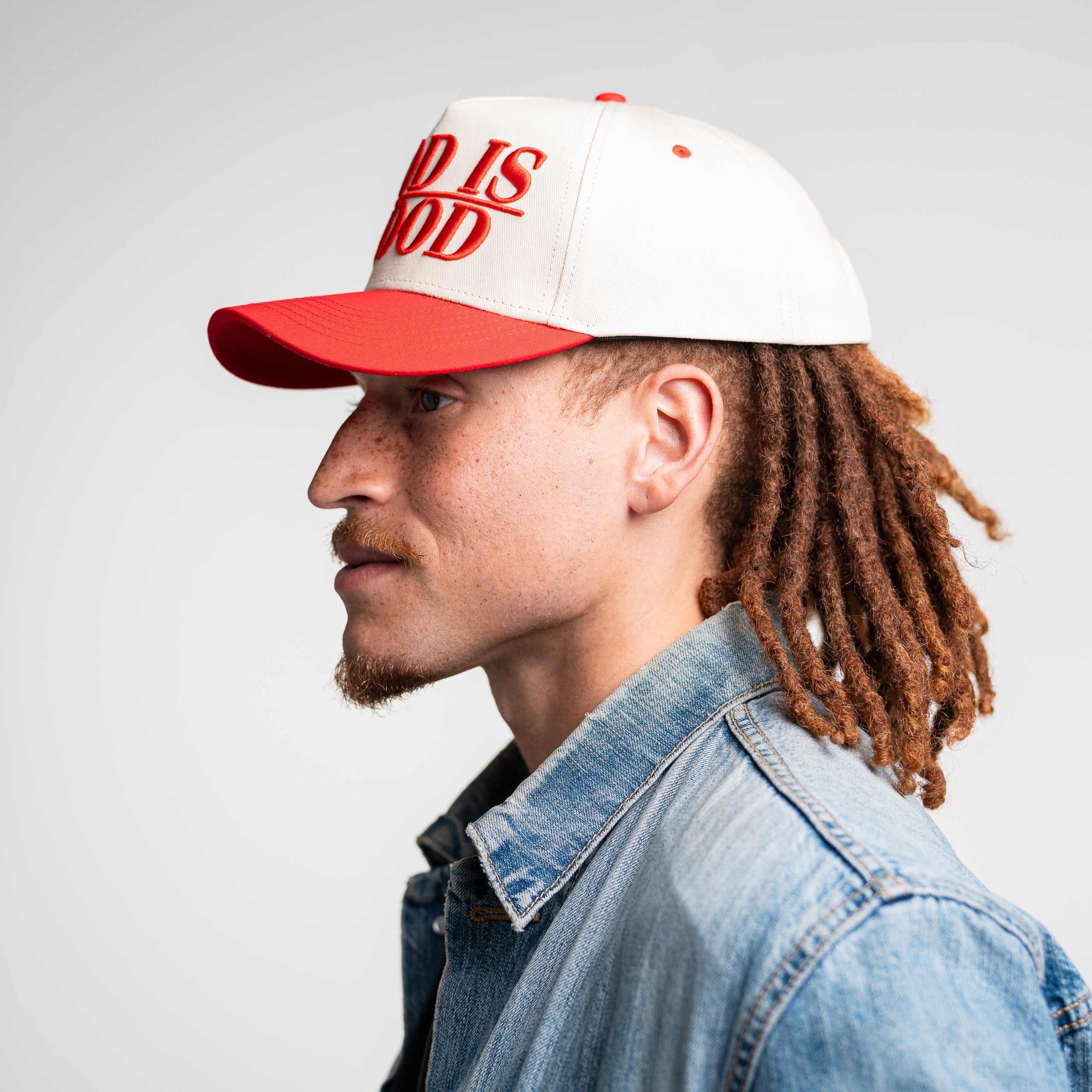 Left side view of man wearing God Is Good Hat, stylish Christian apparel with curved brim and bold message